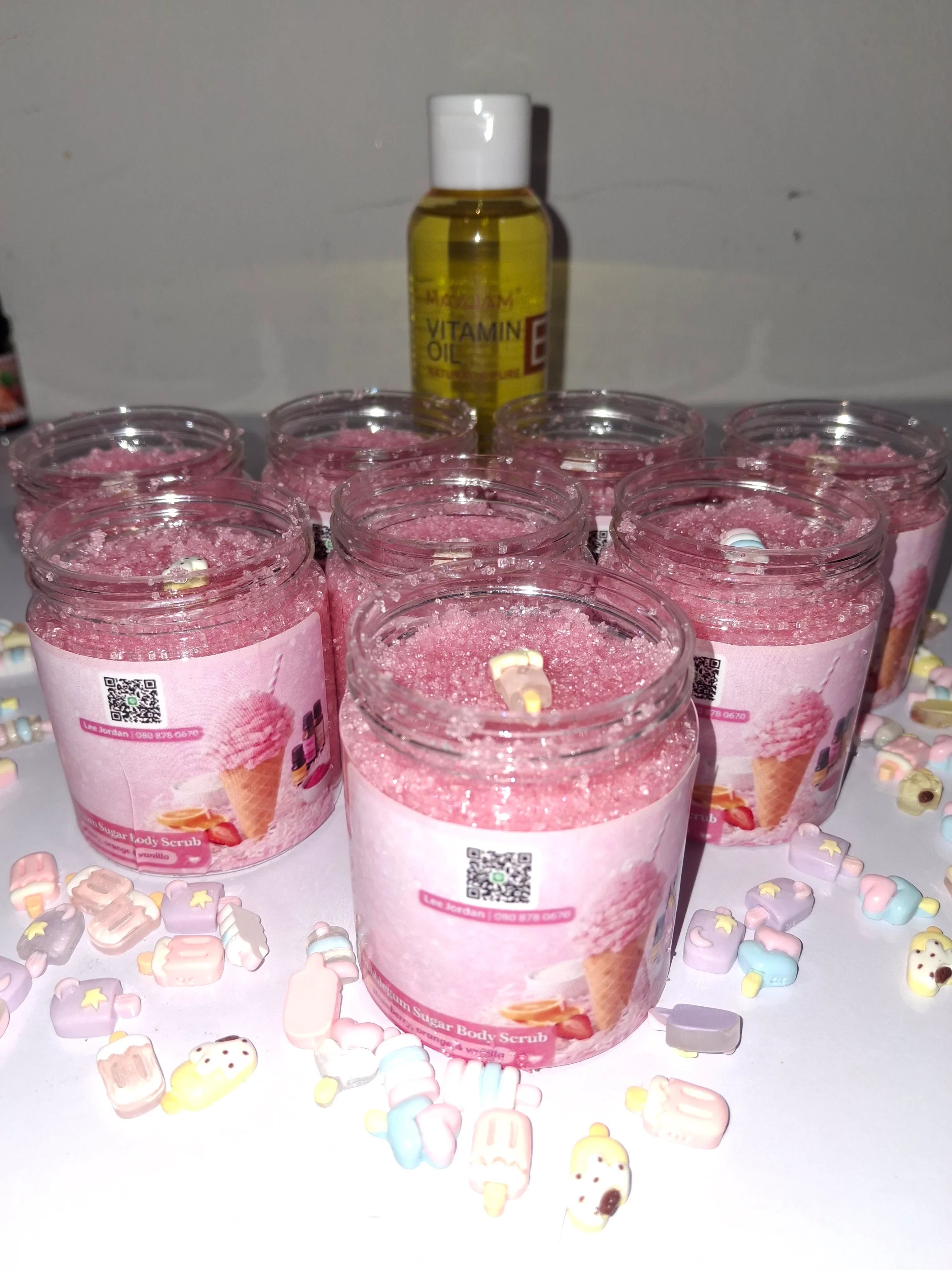 Jars of pink bubble gum body scrub with candy-themed decorations and a bottle of vitamin E oil.