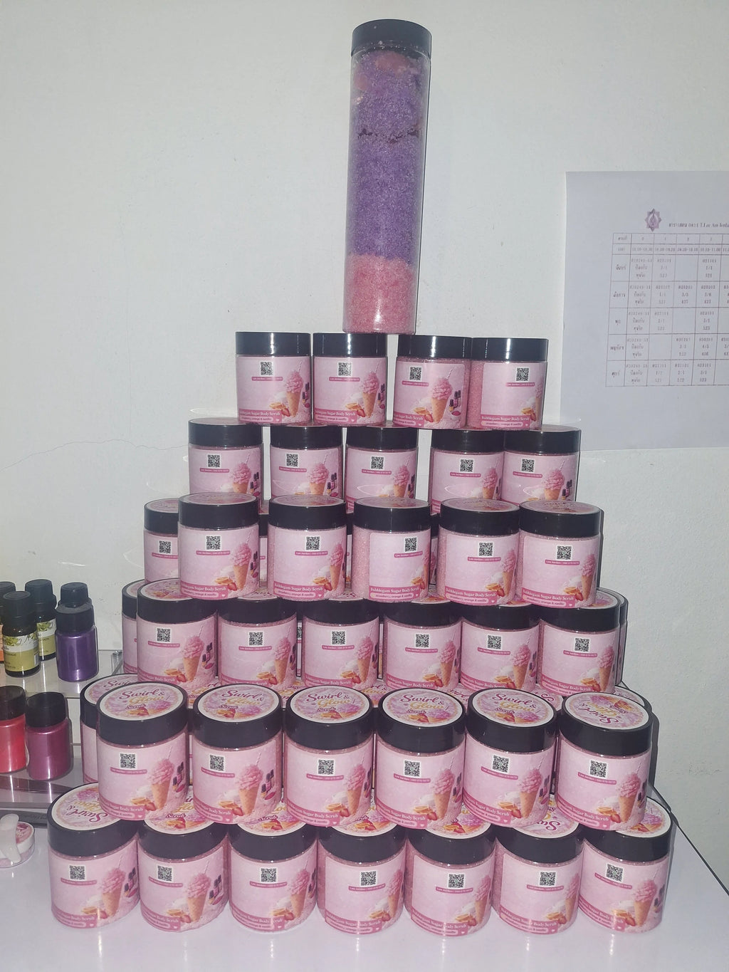 Stacked pink bubble gum body scrub jars with colorful body scrub display on a shelf