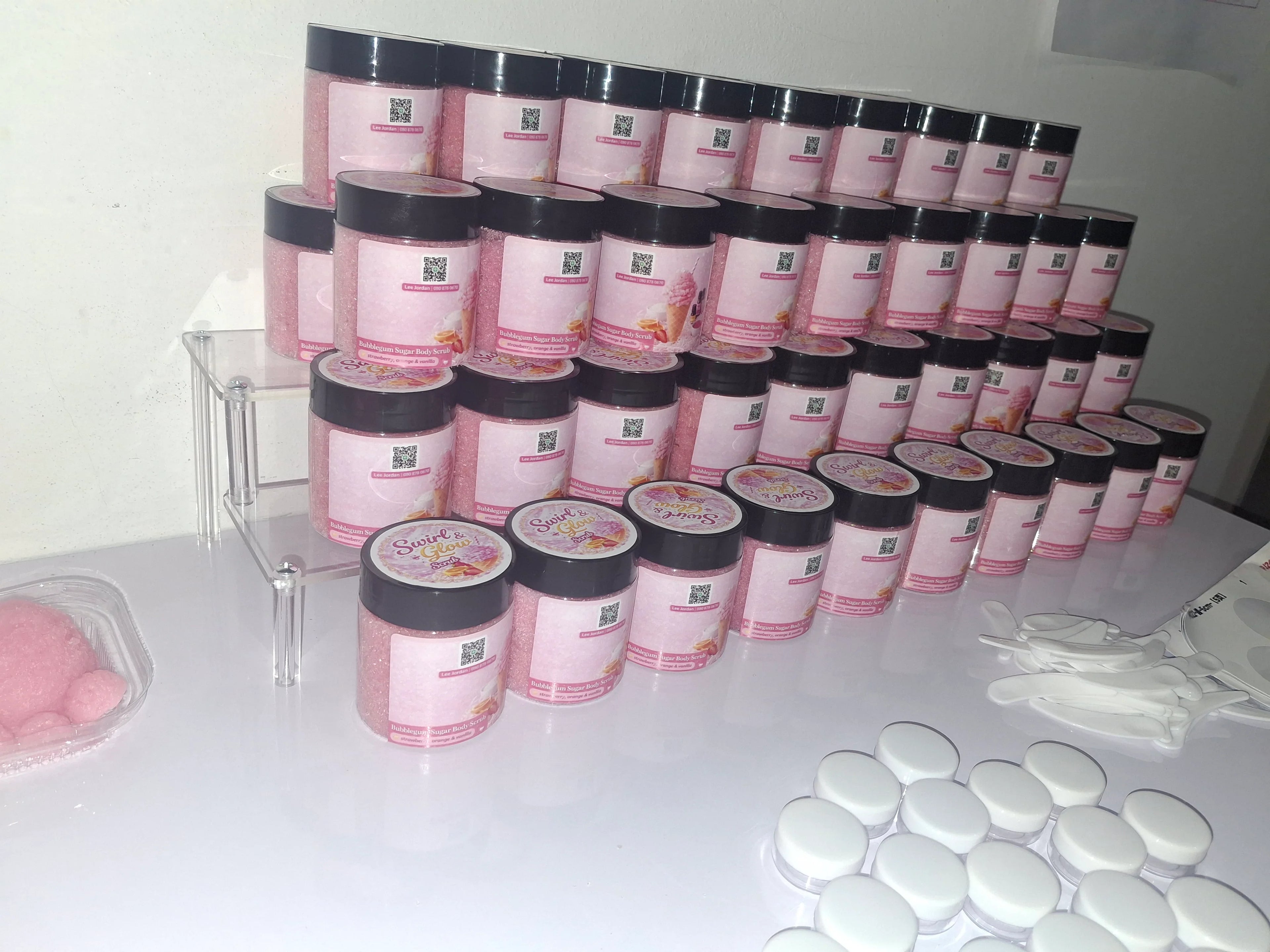 Rows of pink bubble gum body scrub jars with black lids on display table